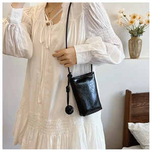 Close-up of black glossy leather crossbody phone bag with knotted tassel and pleated texture
