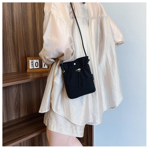 Minimalist black nylon drawstring crossbody bag with slim leather strap shown on model
