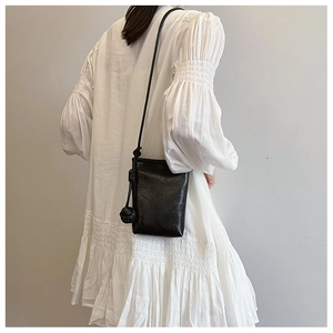 Close-up of minimalist black crossbody bag with knot shoulder strap and wrinkled texture