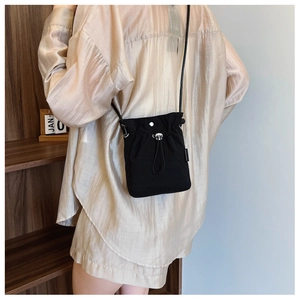 Detail of minimalist black nylon mini crossbody bag showing drawstring and snap closure