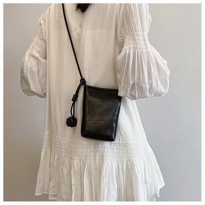 Minimalist black leather crossbody phone bag with knot strap detail on white dress