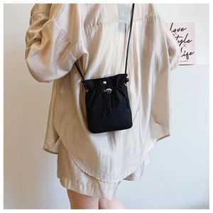 Detail of black drawstring bucket bag with silver metal snap button and slim strap