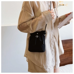 Detail of black drawstring bucket bag with silver metal lock and woven label on shoulder strap