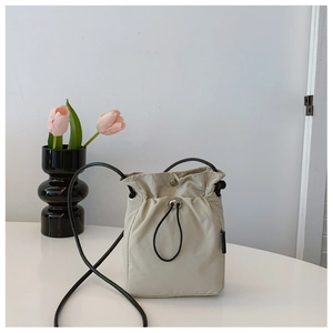 Detail of off-white nylon drawstring bucket bag with black strap and metallic eyelets