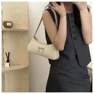 Detail of cream white faux leather shoulder bag featuring a silver metal bow accent