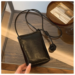 Detail of black glossy phone crossbody bag with vintage oil wax texture and knot strap