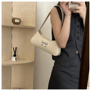 Detail of cream white faux leather underarm bag with silver bow buckle in a lifestyle setting