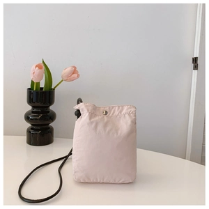 Detail of light pink nylon phone bag with silver snap button and thin black cord strap