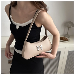 Close-up of a beige underarm bag featuring a metallic silver bow accent on the front