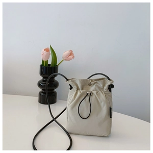 Detail of beige nylon drawstring crossbody bag with black cord strap and magnetic closure