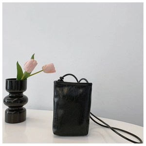 Minimalist black oil-wax leather mini crossbody phone bag shown in a stylish setup
