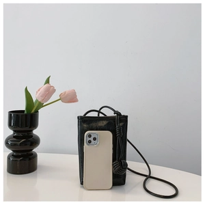 Detail of black leather mini crossbody bag with knotted strap next to phone for scale