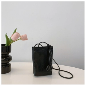 Detail of minimalist black glossy mini crossbody bag with a large decorative knot on strap