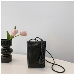 Close-up of black pleated leather phone bag with unique woven ball ornament and slim strap