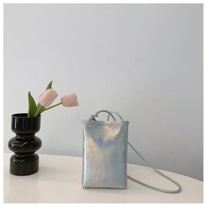 Close-up of holographic silver mini crossbody phone bag with thin strap on white table