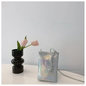 Detail view of silver holographic mini crossbody phone bag with braided rope strap on white desk