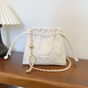 Sac seau matelassé blanc avec bandoulière chaîne dorée sur table en bois