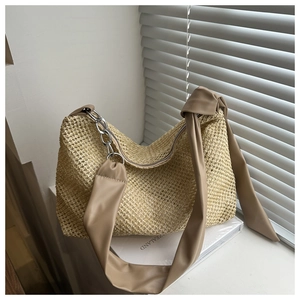 Close-up of woven straw tote bag with brown leather shoulder strap and silver chain detail