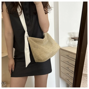 Detail of woven straw tote bag featuring thick fabric shoulder strap and knotted design