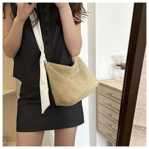 Detail of hand-woven straw tote bag with white fabric strap and decorative knot