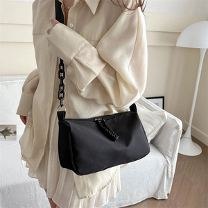 Minimalist black nylon crossbody bag with chunky chain strap worn over a cream shirt