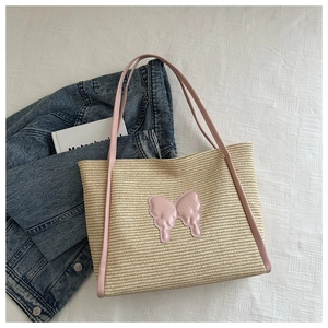 Close-up of woven straw tote bag featuring a pink leather bow and slim shoulder strap