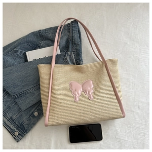 Detail of woven straw tote bag with pink leather butterfly patch and top handles