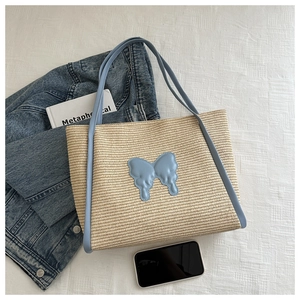 Detail of straw tote bag with light blue leather trim and butterfly patch on fabric