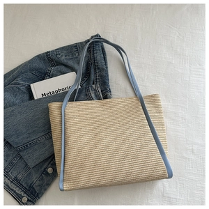 Detail of hand-woven straw tote bag featuring light blue faux leather trims and handles