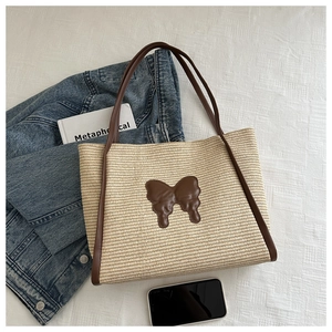 Detail of hand-woven straw tote bag with brown leather butterfly patch and long shoulder straps