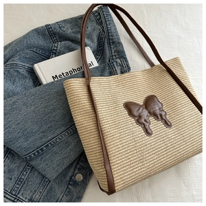 Detail of woven straw tote bag featuring a leather butterfly patch and brown straps
