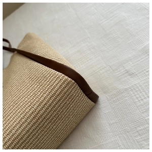 Detailed view of the woven straw tote bag base with dark brown leather piping trim