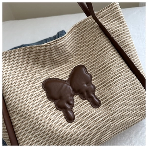 Close-up of woven straw tote bag with brown leather butterfly patch and shoulder strap