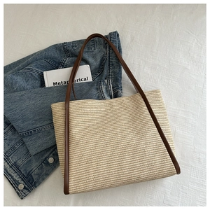 Detail of hand-woven straw tote bag featuring brown leather trim and sturdy handles