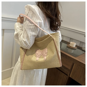 Detail view of large straw tote bag with pink butterfly patch worn on shoulder