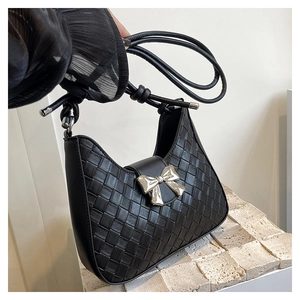 Detail of black woven shoulder bag with elegant silver metallic bow charm and leather strap