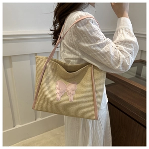Detail of straw tote bag with pink butterfly patches and leather straps for summer beach use