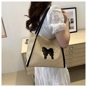 Detail view of woven straw tote bag featuring a black butterfly applique and shoulder straps