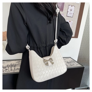 Detail of a creamy woven underarm bag featuring a metallic silver bow clasp with strap