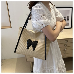 Straw tote bag with black butterfly patch shown on a model in a minimalist room