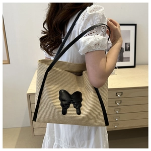 Detail of hand-woven tote bag with black bow leather patch and long shoulder straps