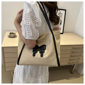 Detail view of woven straw tote bag featuring a leather bow and slender shoulder strap