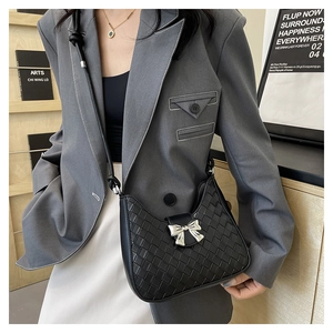 Detail of black woven shoulder bag featuring a silver bow-knot buckle and crescent shape