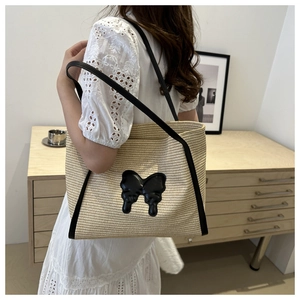 Detail of hand-woven straw tote with black leather butterfly patch and shoulder straps