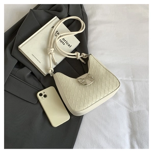 Detail of cream woven shoulder bag featuring a silver metal bow buckle and textured finish