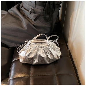 Detailed view of silver metallic pleated cloud bag on a black textured leather bench