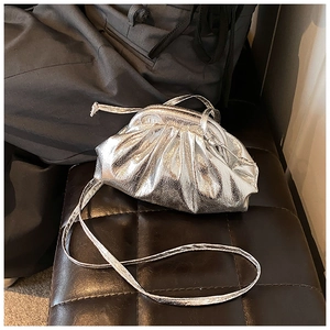 Detailed view of silver metallic pleated cloud bag on a leather texture background