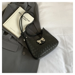 Detail of woven crescent bag with a silver metal bow accent against a grey suit