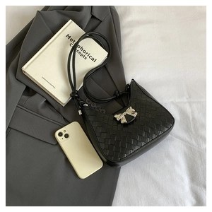 Close-up of black woven underarm bag with silver bow buckle and knotted strap details
