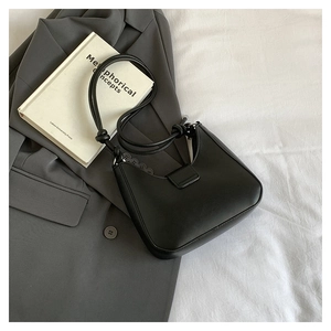 Detail of matte black underarm bag with knot handle placed on a dark grey blazer